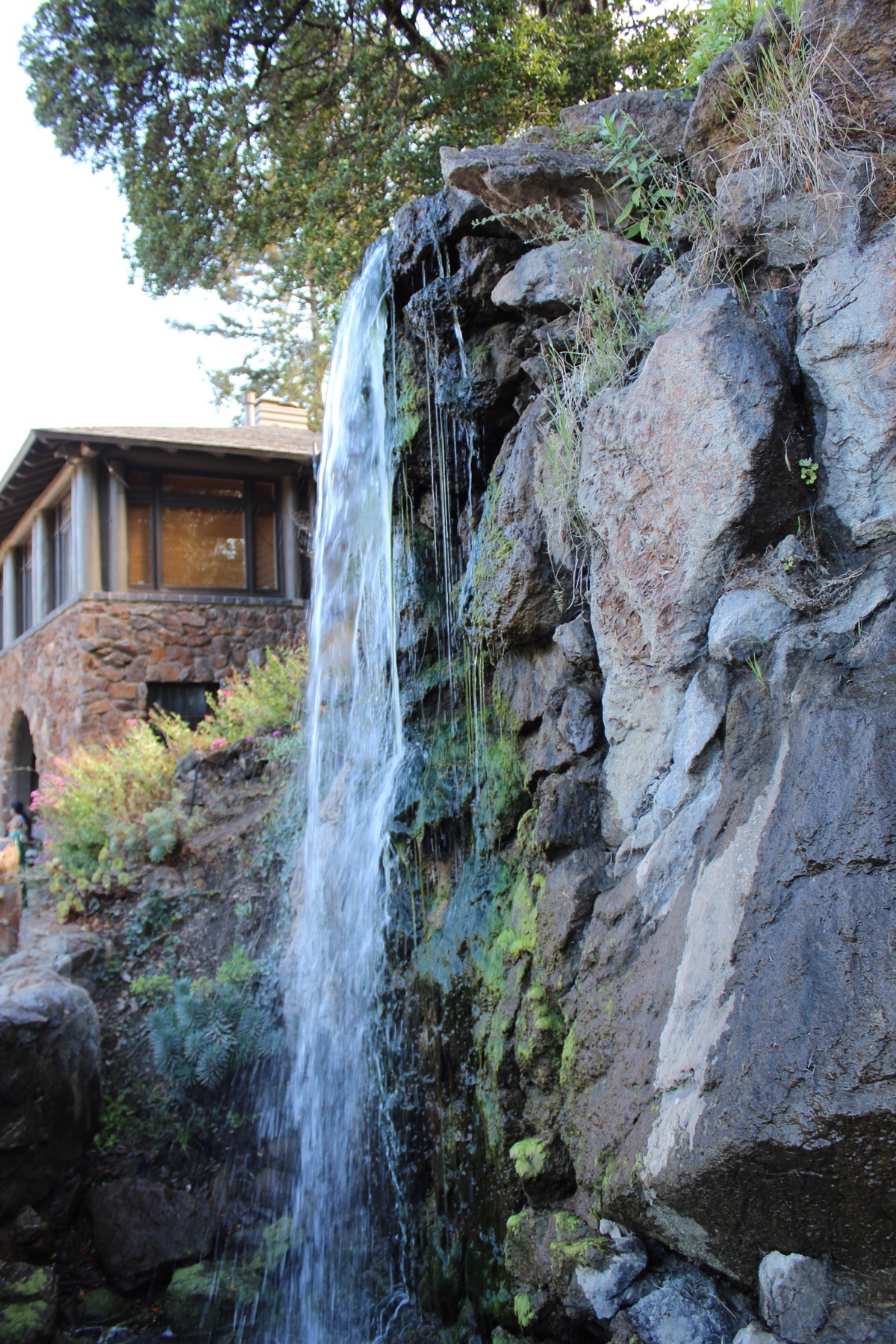 Water falling over a rock wall beside a rustic stone building